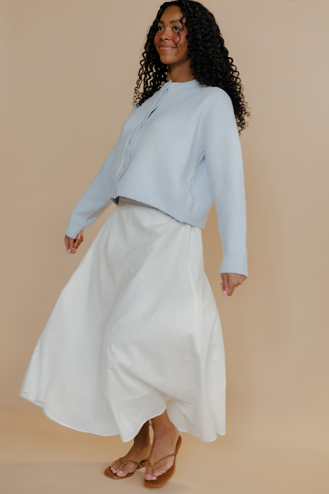 Woman wearing a light blue top and white skirt against a beige background