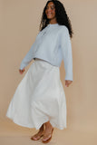 Woman wearing a light blue top and white skirt against a beige background
