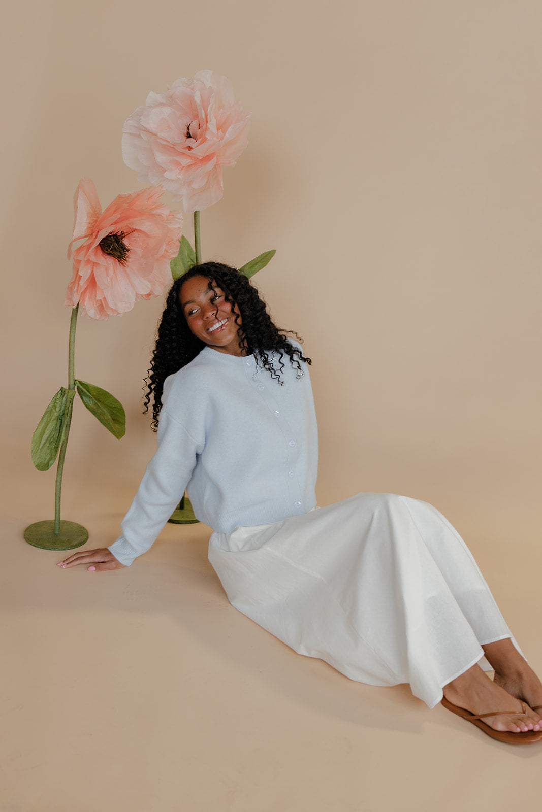 Woman sitting on a beige floor with large flowers behind her