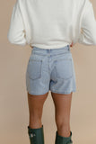 Person wearing light blue denim shorts and green rain boots on a beige background