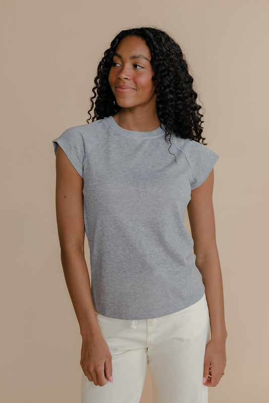 Woman wearing a gray t-shirt and white pants against a beige background
