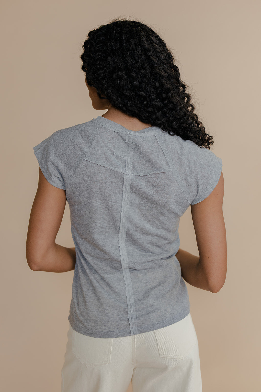 Woman wearing a gray short-sleeve top and white pants against a beige background
