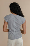 Woman wearing a gray short-sleeve top and white pants against a beige background