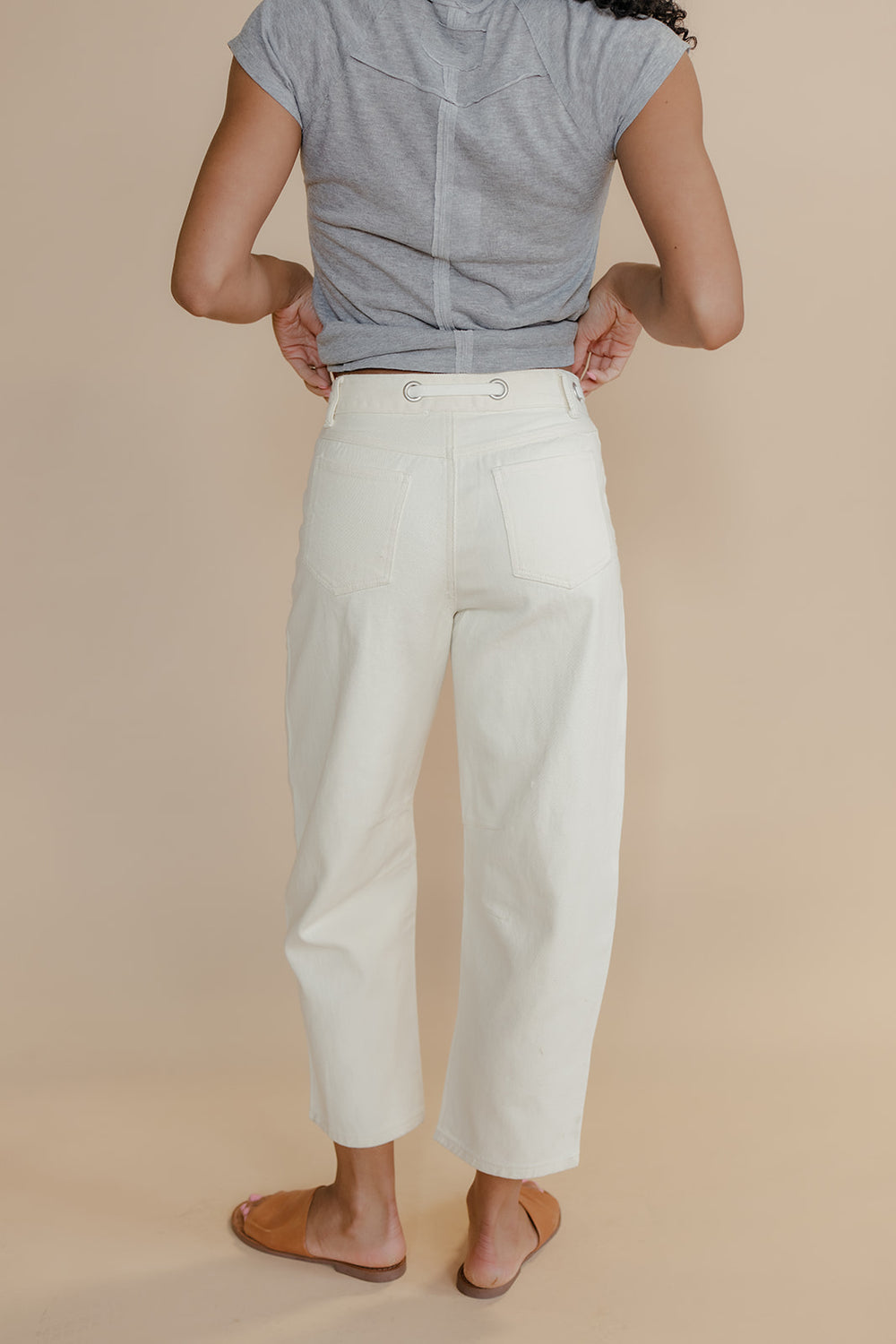 Person wearing a light gray sleeveless top and white pants on a beige background