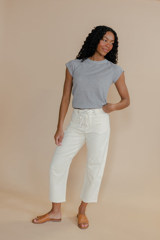 Woman wearing a gray top and white pants against a beige background