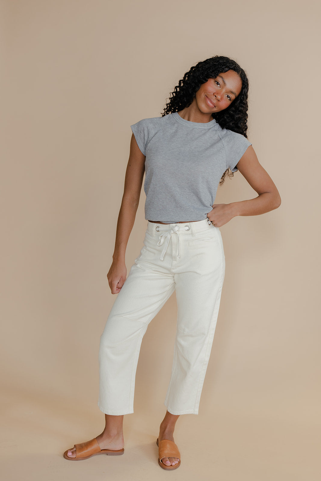 Woman wearing a gray top and white pants against a beige background