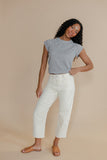 Woman wearing a gray top and white pants against a beige background