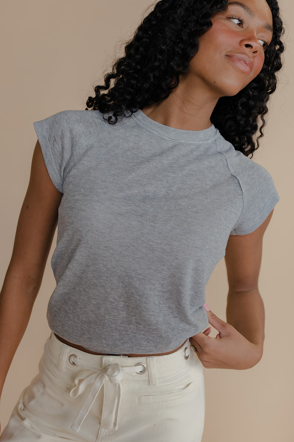 Woman wearing a gray t-shirt and white pants against a beige background