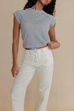 Woman wearing a gray top and white pants against a beige background