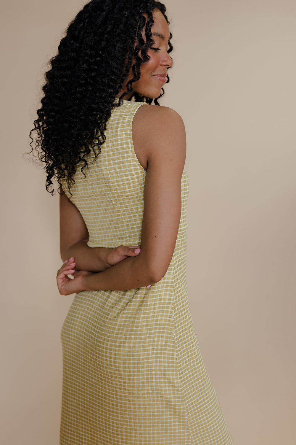 Woman wearing a yellow checkered dress against a beige background
