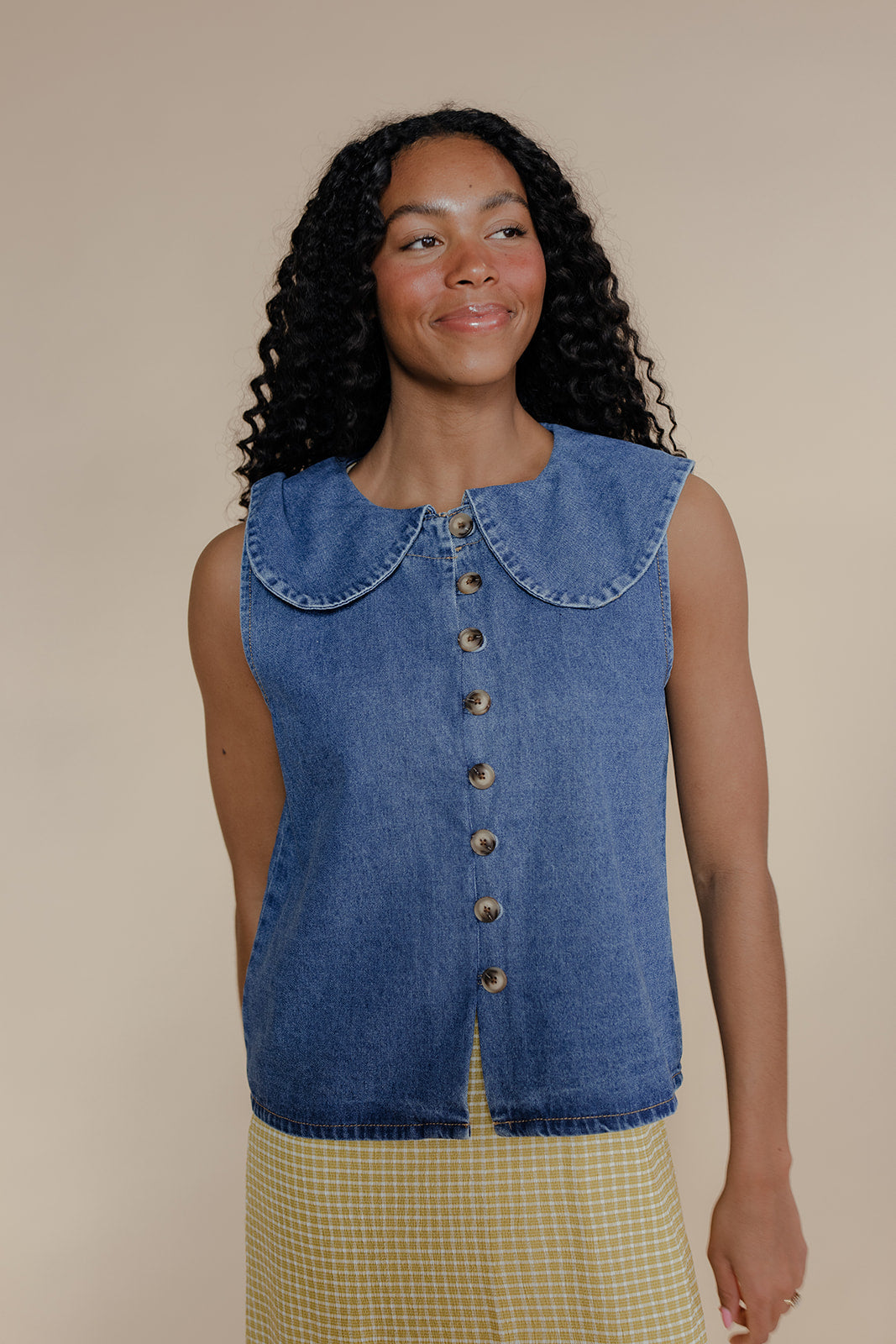 Woman wearing a blue denim vest with a beige background