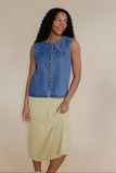 Woman wearing a blue denim vest over a yellow checkered dress on a beige background
