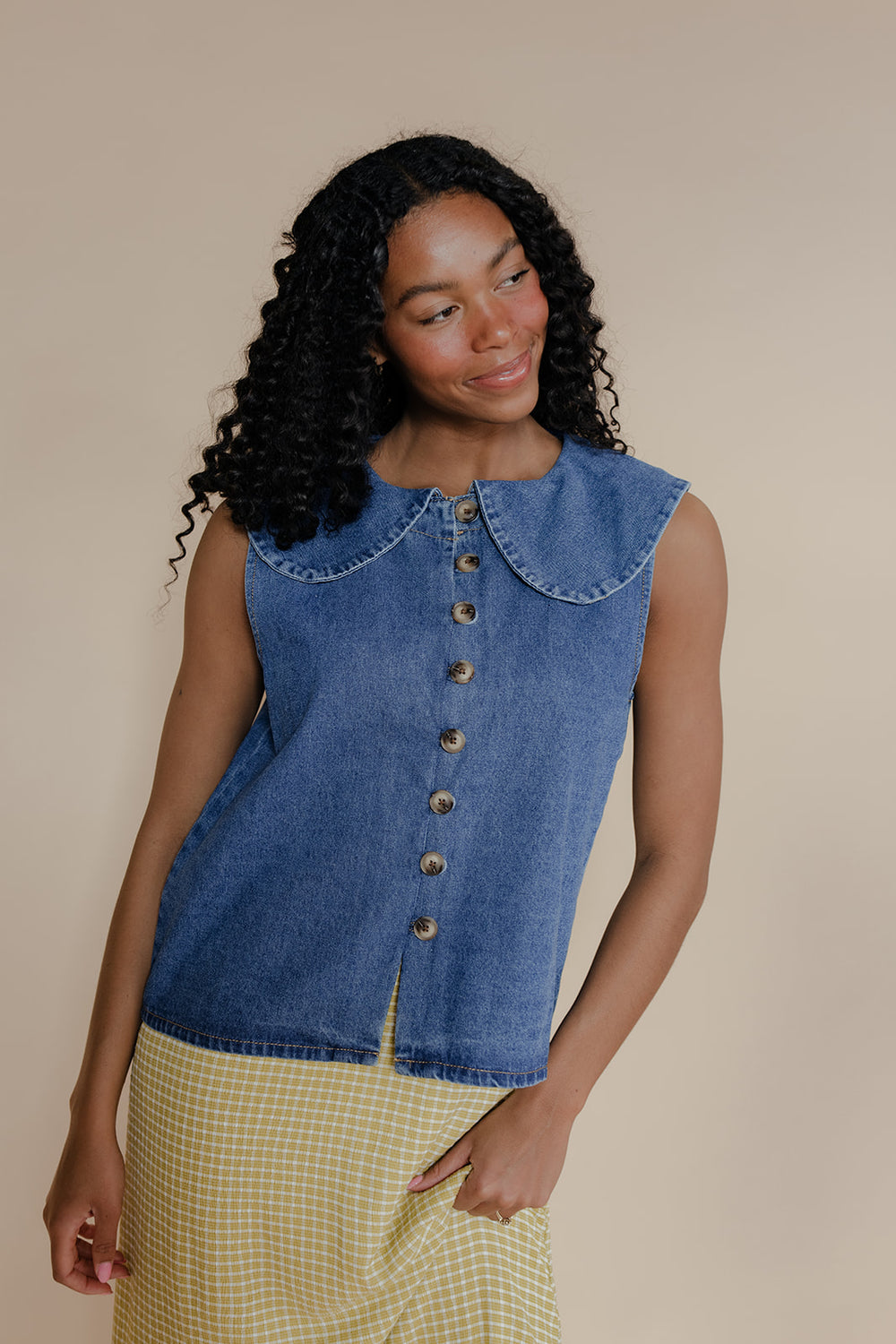 Woman wearing a denim sleeveless top with a beige background