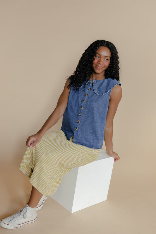 Woman wearing a denim vest over a yellow dress on a beige background