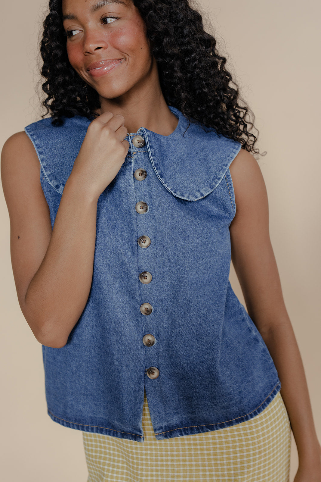Woman wearing a blue denim vest against a beige background