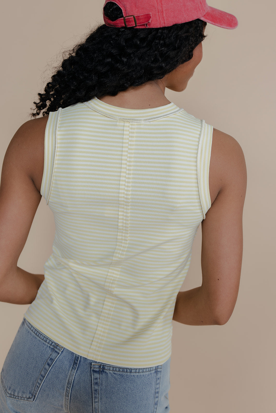 Person wearing a light green striped tank top and pink cap on a beige background