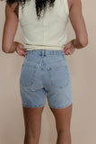 Person wearing a yellow striped tank top and blue denim shorts on a beige background