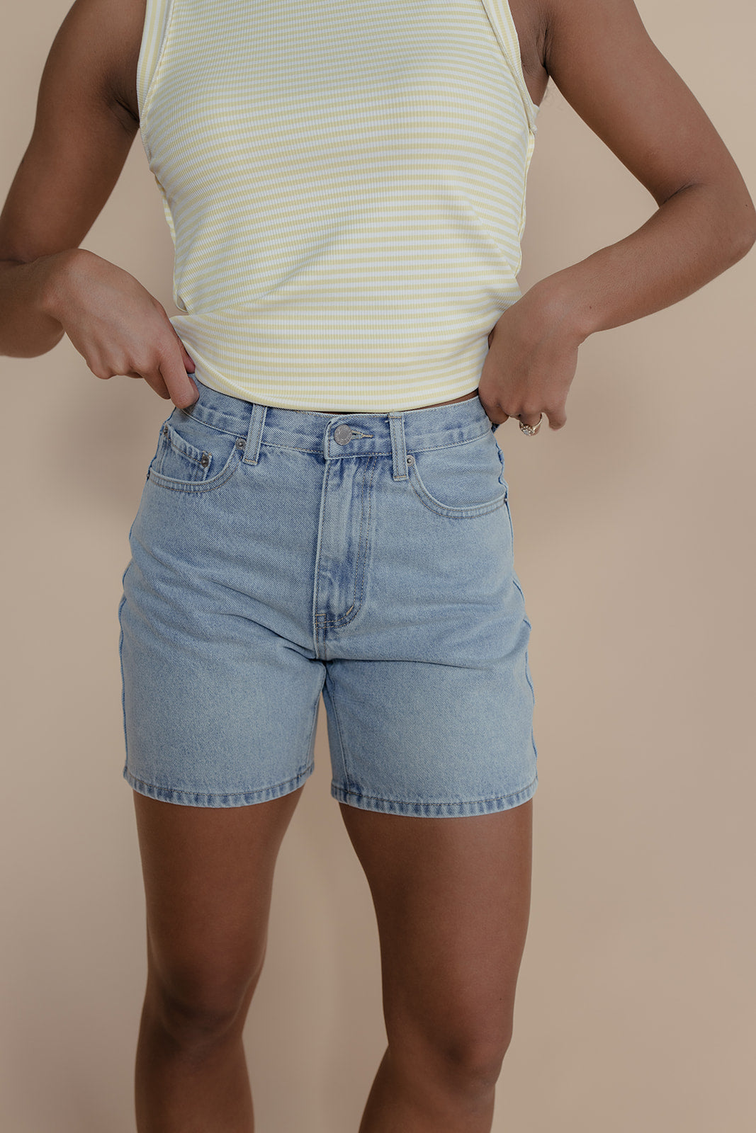 Person wearing a striped tank top and denim shorts on a beige background