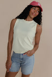 Woman wearing a light green tank top, blue shorts, and a pink cap with a logo on a beige background