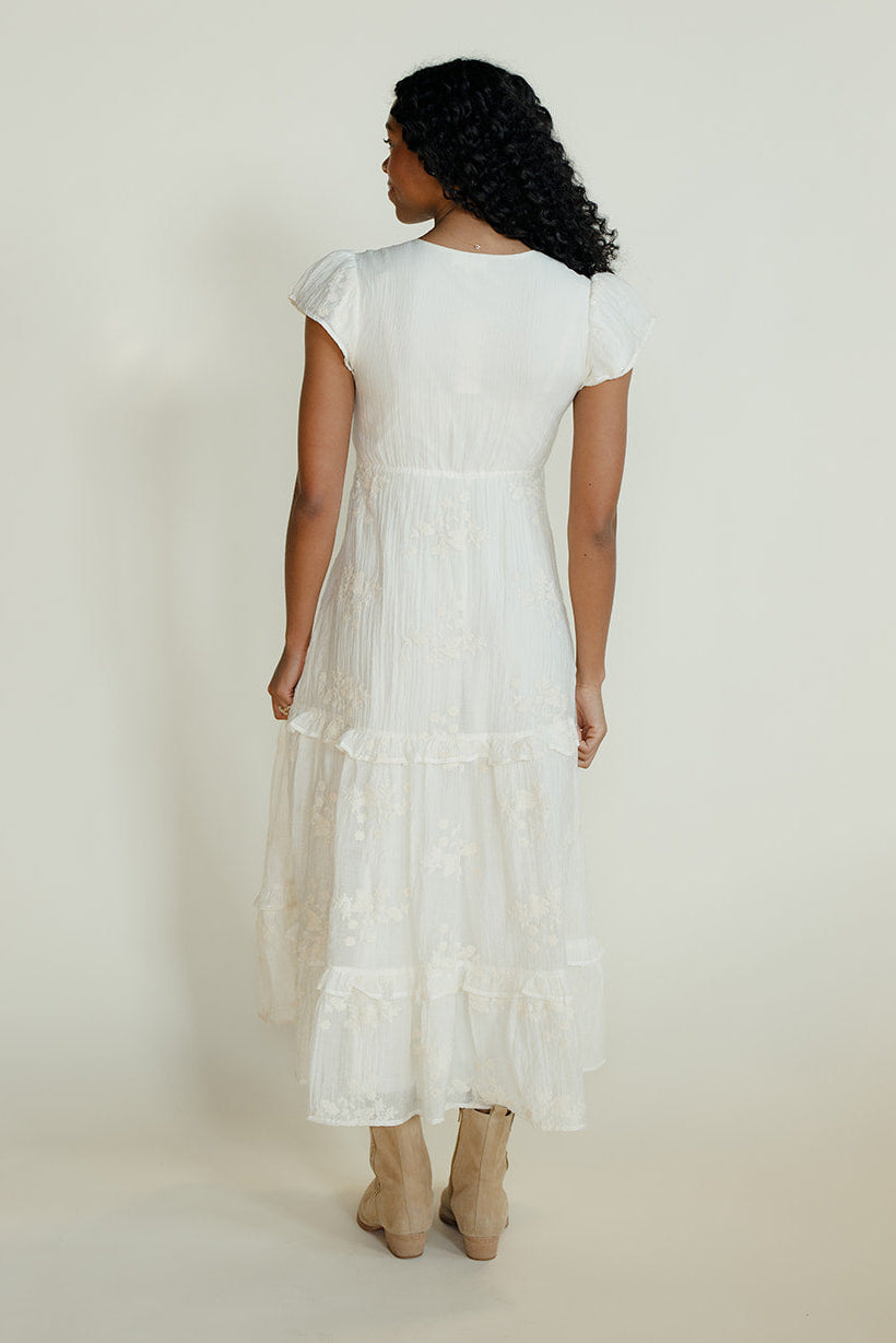 Woman wearing a white dress with ruffled sleeves and bottom hem on a plain background