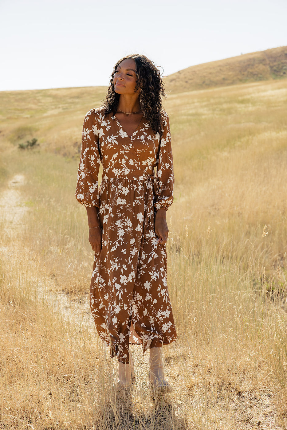 a woman in a brown dress standing in a field