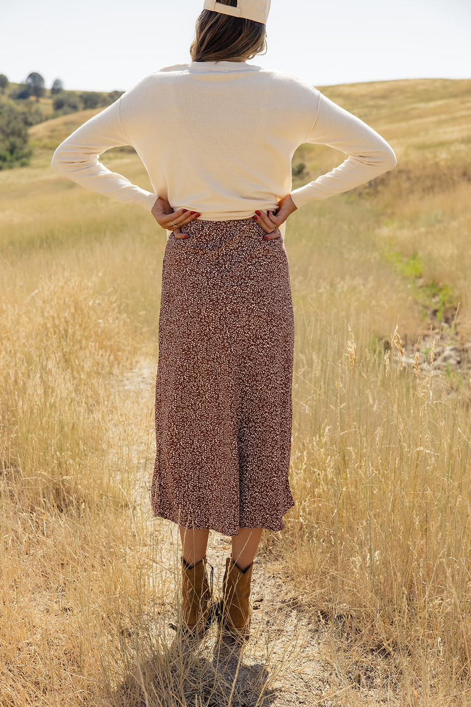 a woman in a skirt and boots standing in a field