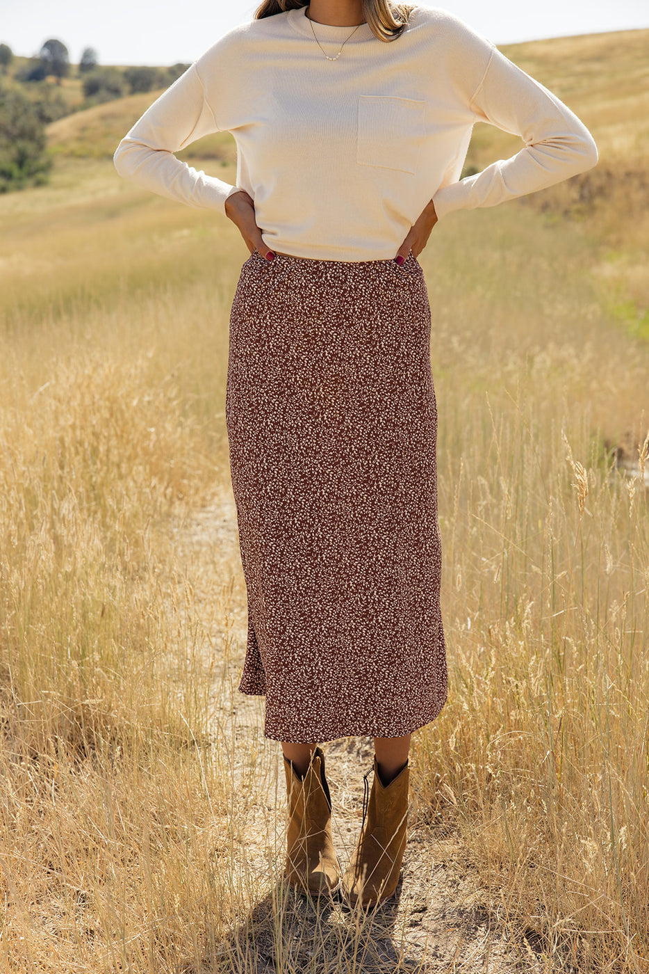 a woman in a long skirt and boots standing in a field