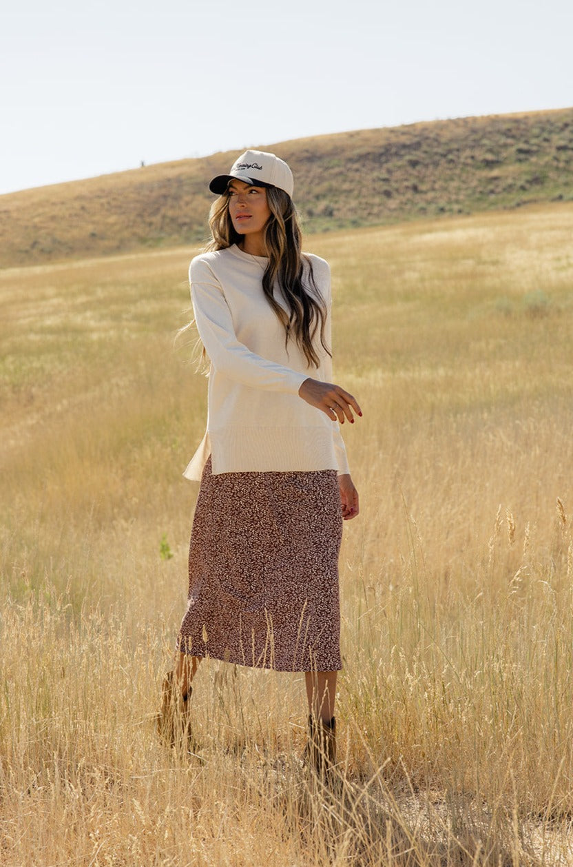 a woman in a long skirt and a white hat standing in a field