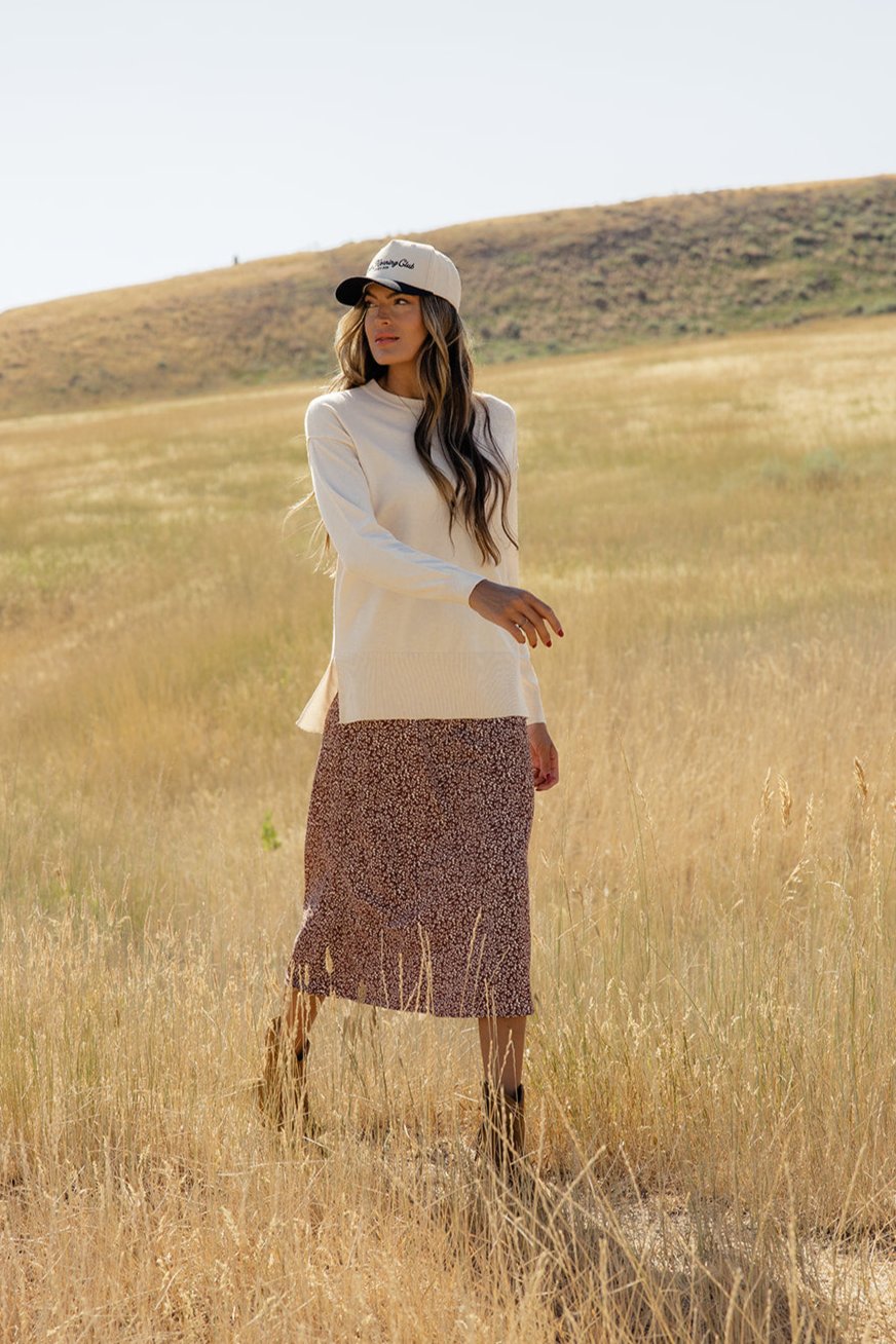 a woman in a hat and long hair standing in a field of tall grass