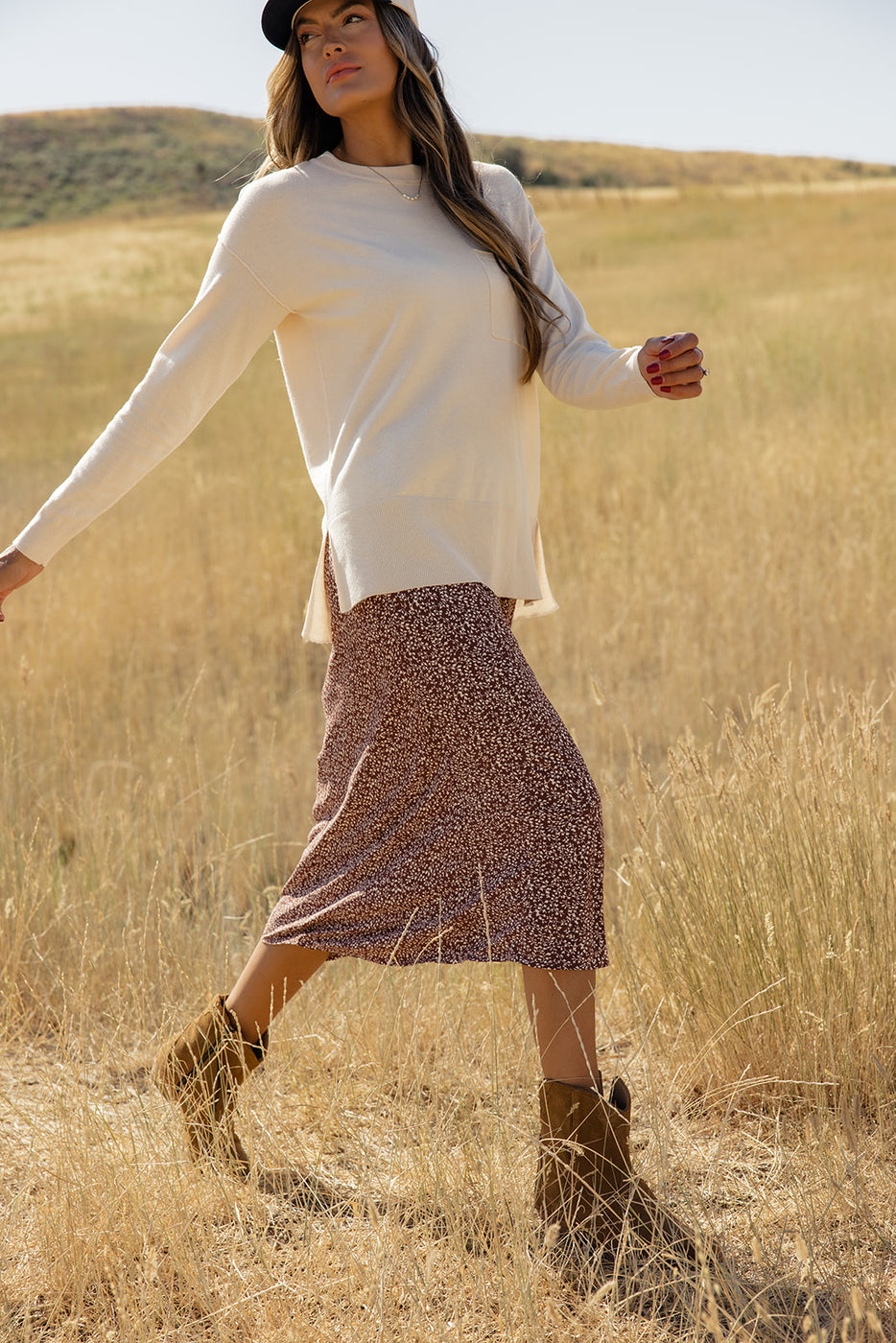 a woman in a skirt and boots walking in a field