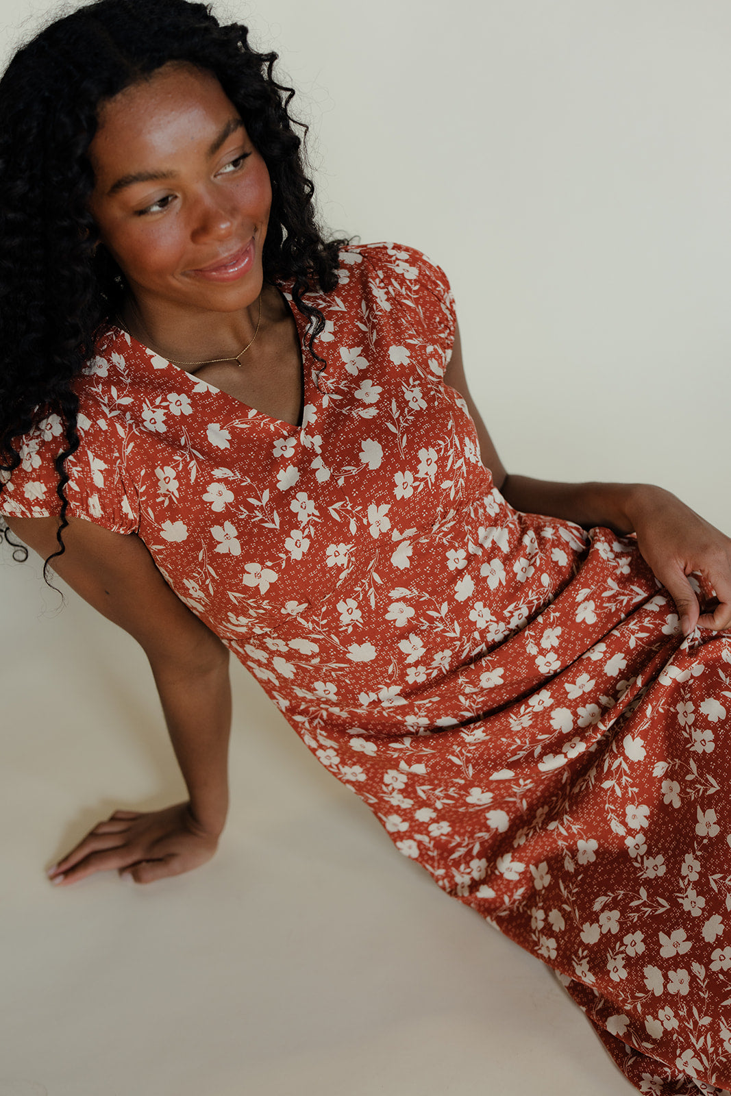 Woman wearing a red floral dress sitting on a white background