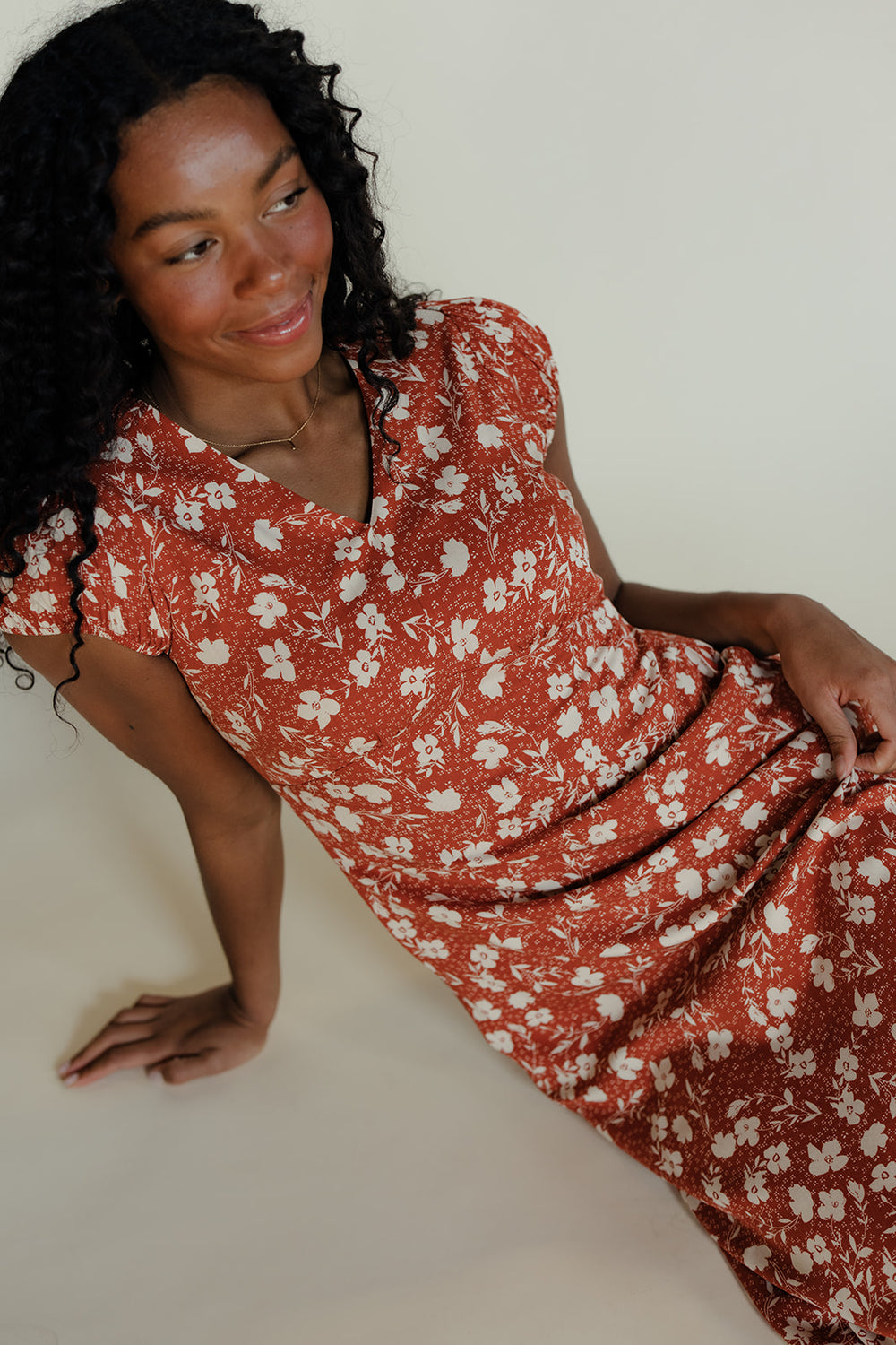 Woman wearing a red floral dress sitting on a white background