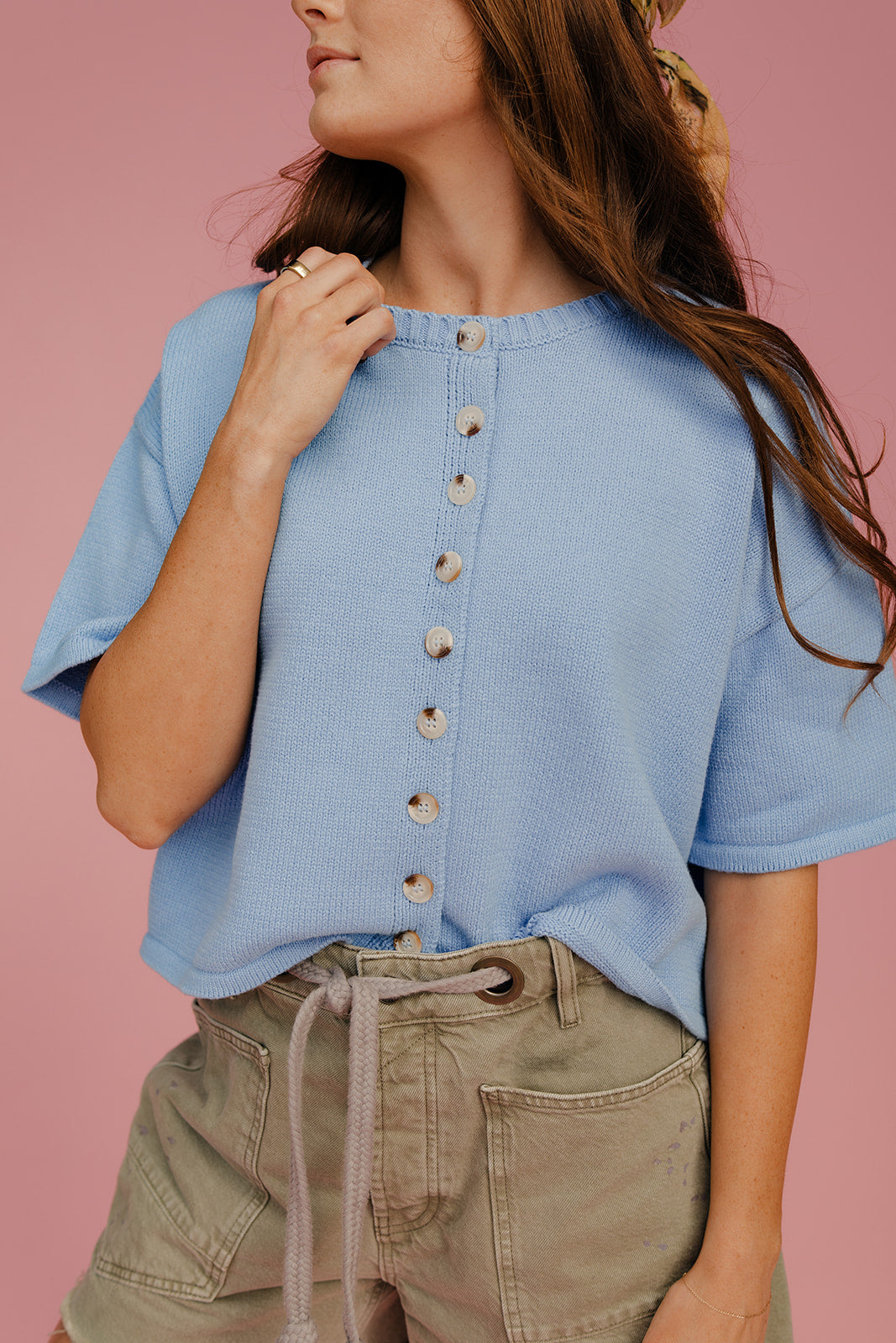 Woman wearing a light blue button-up shirt and green shorts against a pink background