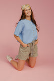 Woman wearing a blue shirt and beige shorts on a pink background