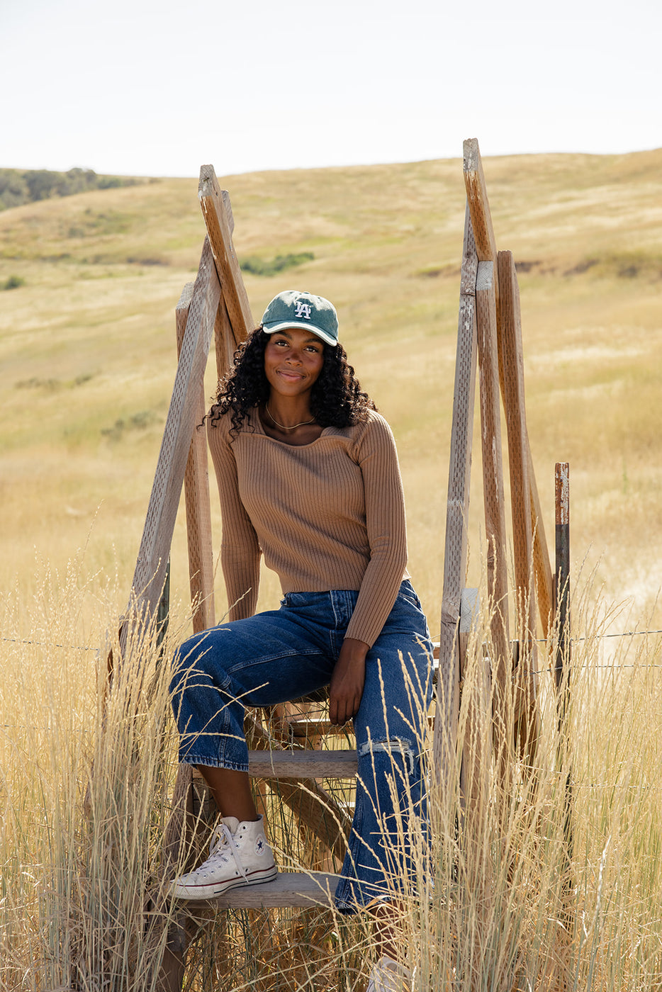 a woman sitting on a wooden ladder in a field