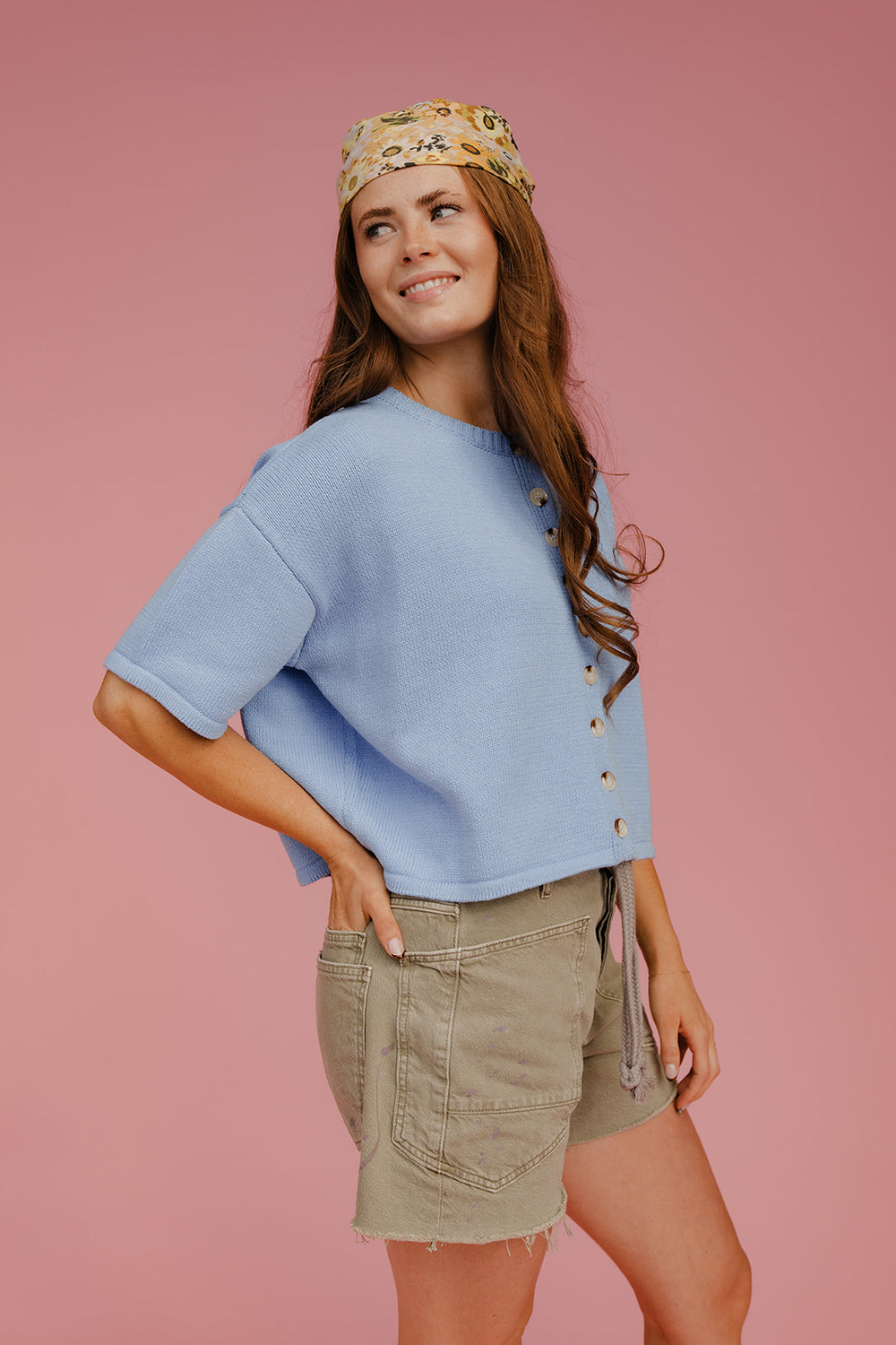 Woman wearing a blue top and beige shorts with a headband against a pink background