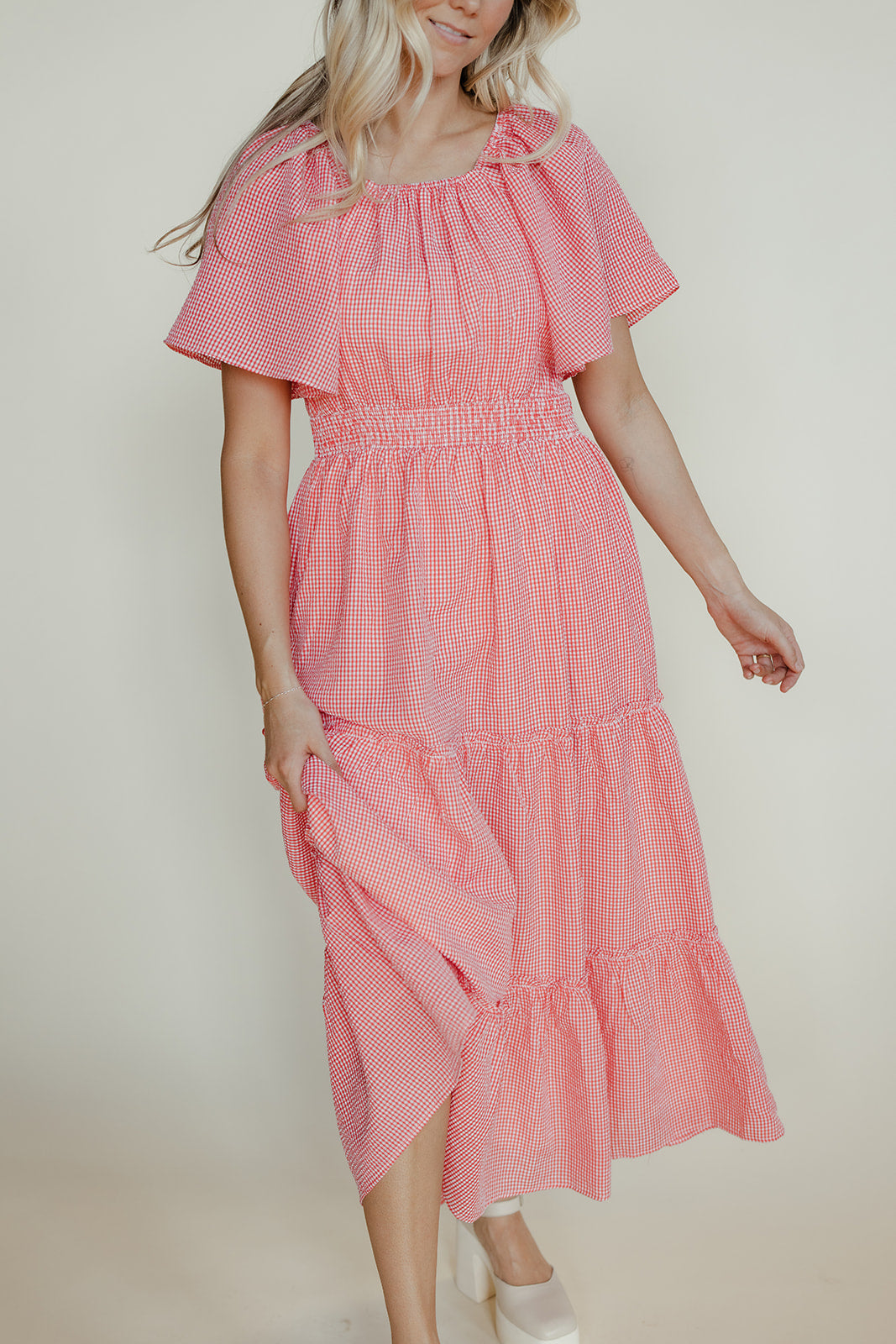 Woman wearing a pink checkered dress against a plain background