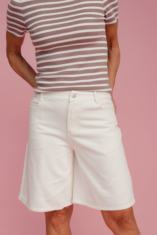 Person wearing a striped shirt and white shorts on a pink background
