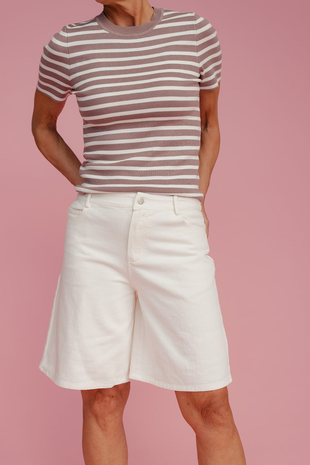 Person wearing a striped shirt and white shorts on a pink background