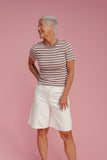 Older woman wearing a striped tee and white shorts on a pink background
