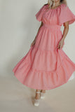 Woman wearing a pink dress with ruffled sleeves and layers on a plain background