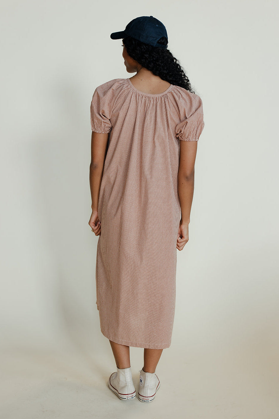 Woman wearing a pink dress and black cap against a white background