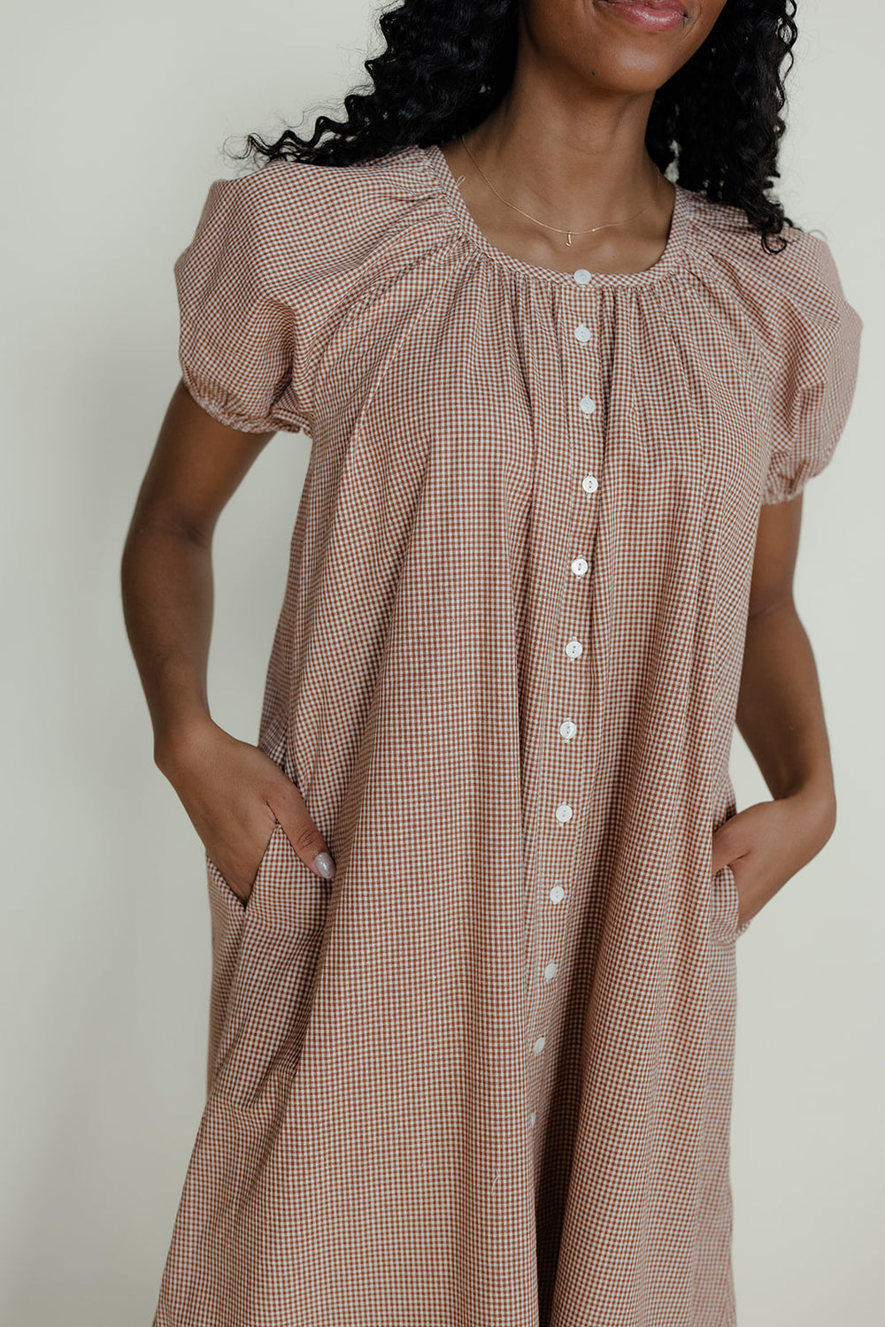 Woman wearing a brown checkered dress with puffed sleeves against a neutral background