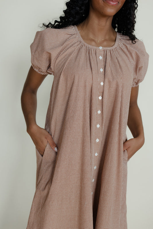 Woman wearing a brown checkered dress with puffed sleeves against a neutral background