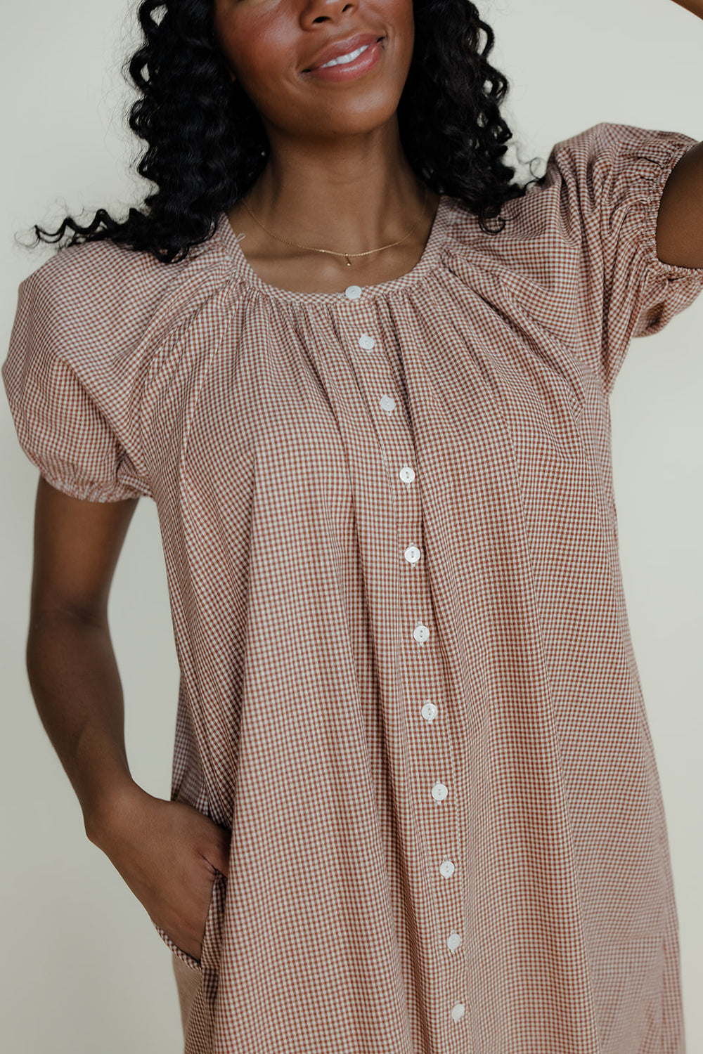Woman wearing a brown checkered dress with white buttons against a plain background