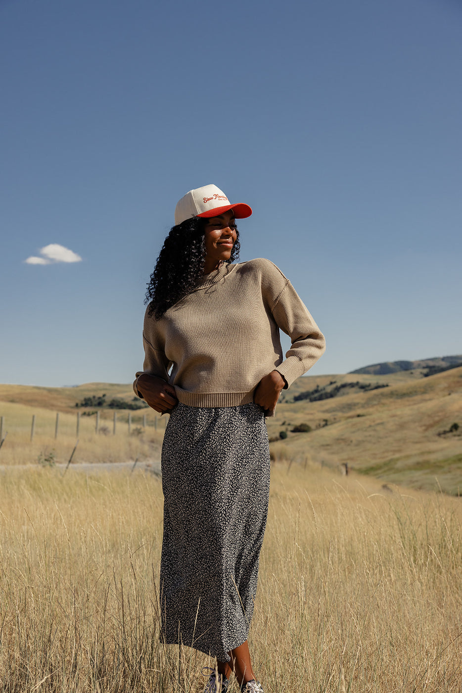 a woman in a long skirt and a hat standing in a field