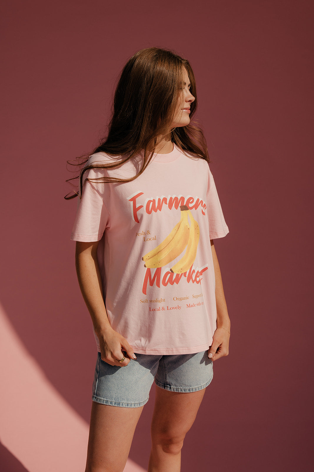 Woman wearing a pink t-shirt with a banana graphic and text against a pink background