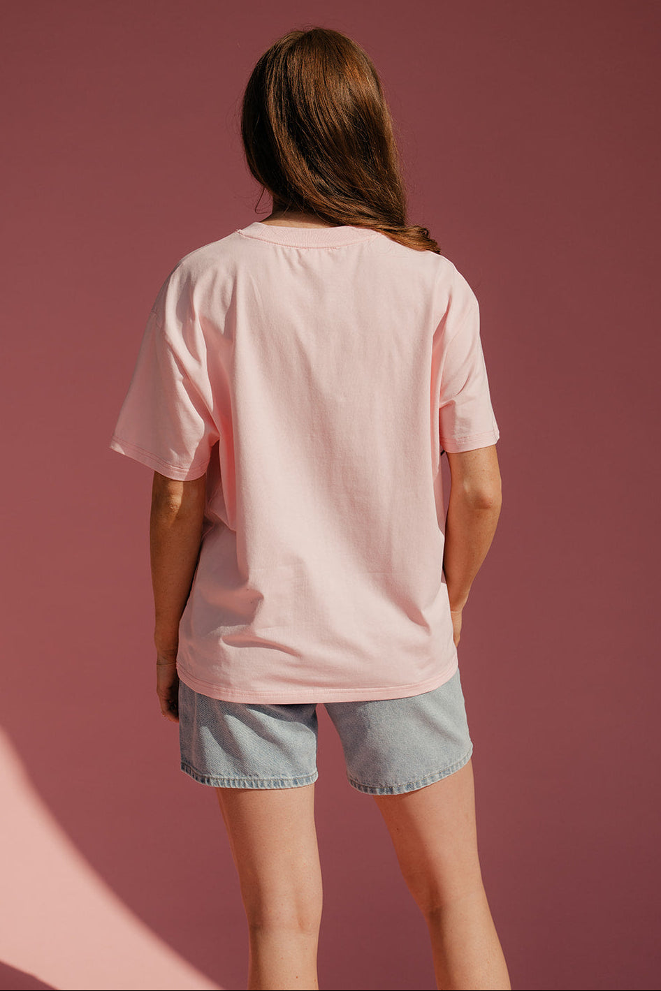 Person wearing a pink oversized t-shirt and denim shorts against a pink background