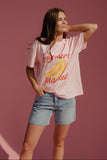 Woman wearing a pink t-shirt with 'Farmers Market' and banana graphic on a pink background