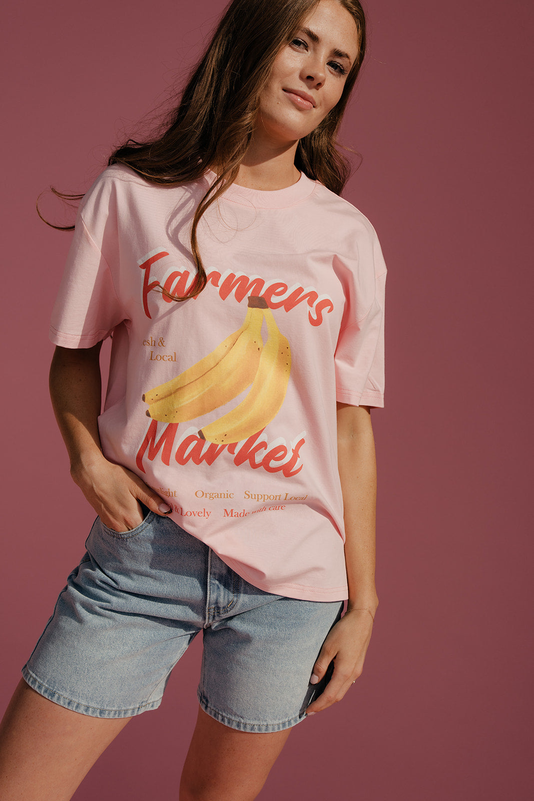 Person wearing a pink t-shirt with 'Farmers Market' and banana graphics on a pink background